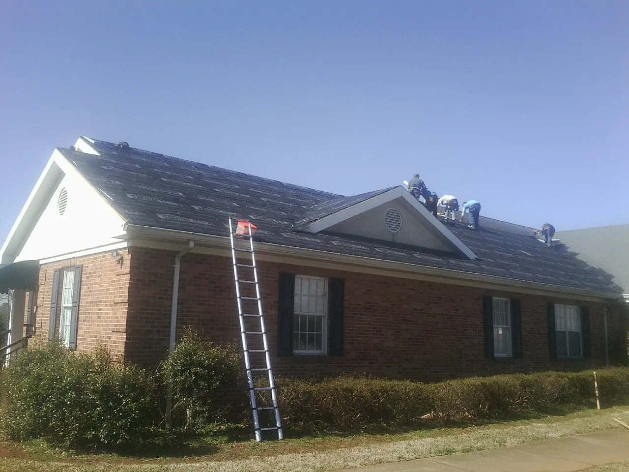 Crew tearing shingles off a brick ranch roof with a ladder set — Metal Roof Repair work by our crew in Wrightsville