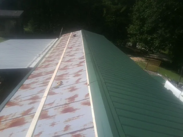 Old rusted panels beside newly installed green metal roofing — Wind Damage Roof Repair by Roofing Brothers in Wrightsville