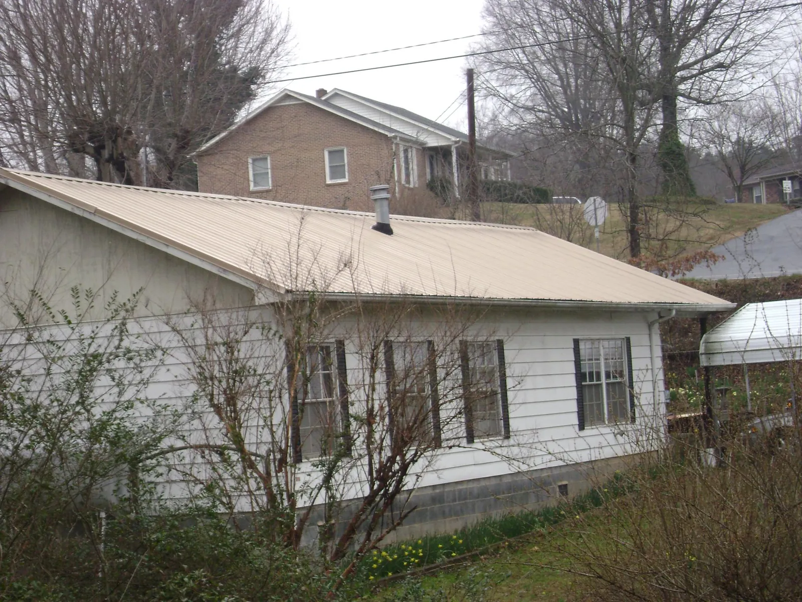 Tan metal roof on a white sided house set into a hillside — Commercial Roofing by Roofing Brothers in Wrightsville